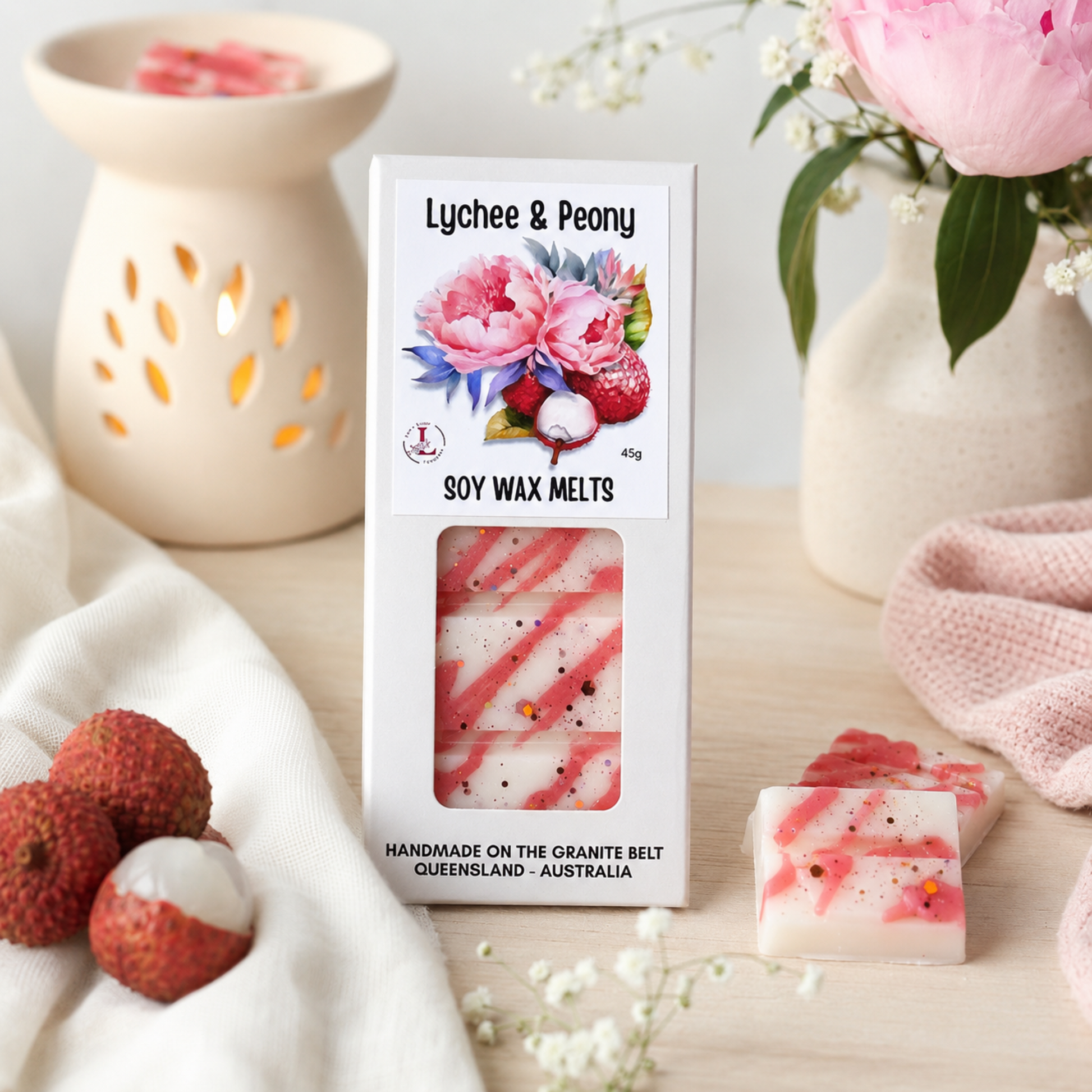 "Lee's Little Luxuries Lychee & Peony Soy Wax Melts displayed in a stylish home setting with a ceramic wax burner, fresh pink peonies, lychee fruit and wax melt cubes, showcasing handmade Australian soy wax melts."